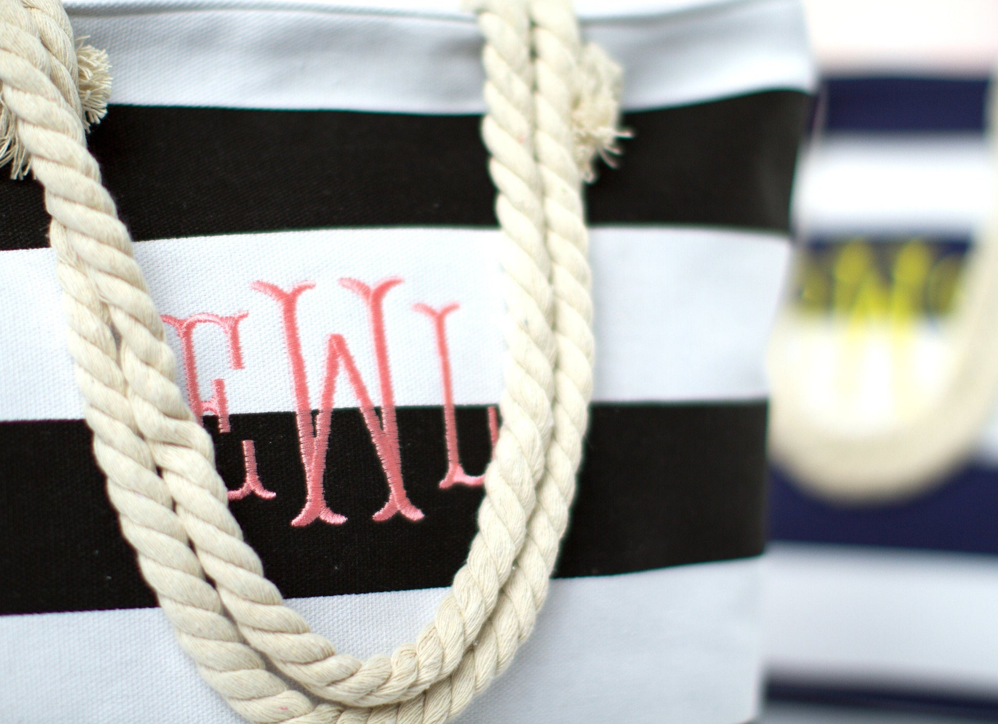 Close-up of the black and white bold stripe tote showing the embroidered script monogram and rope handles