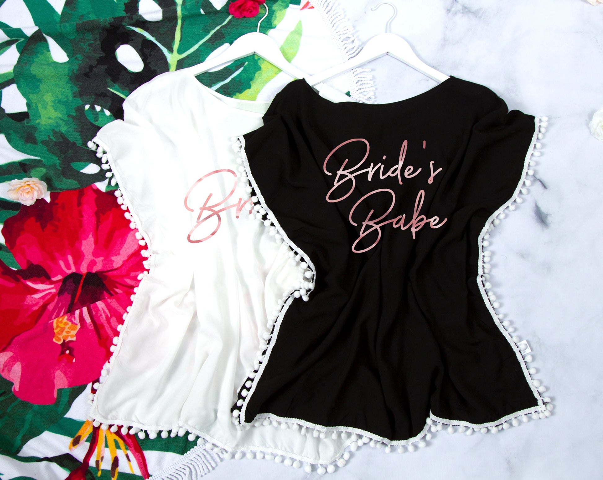 Three cover-ups flat-laid on a tropical floral backdrop, "Bride's Babe" printed in rose gold