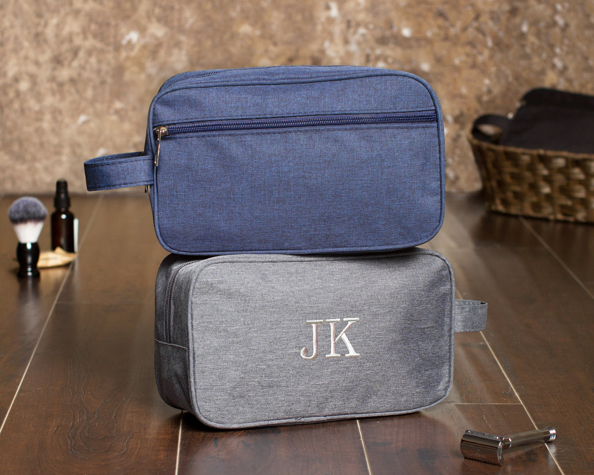 Navy dopp kit stacked on a gray one embroidered "JK", showing the outside zip pocket