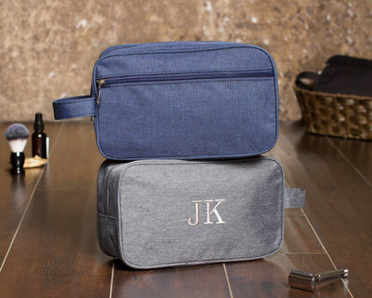 Navy dopp kit stacked on a gray one embroidered "JK", showing the outside zip pocket