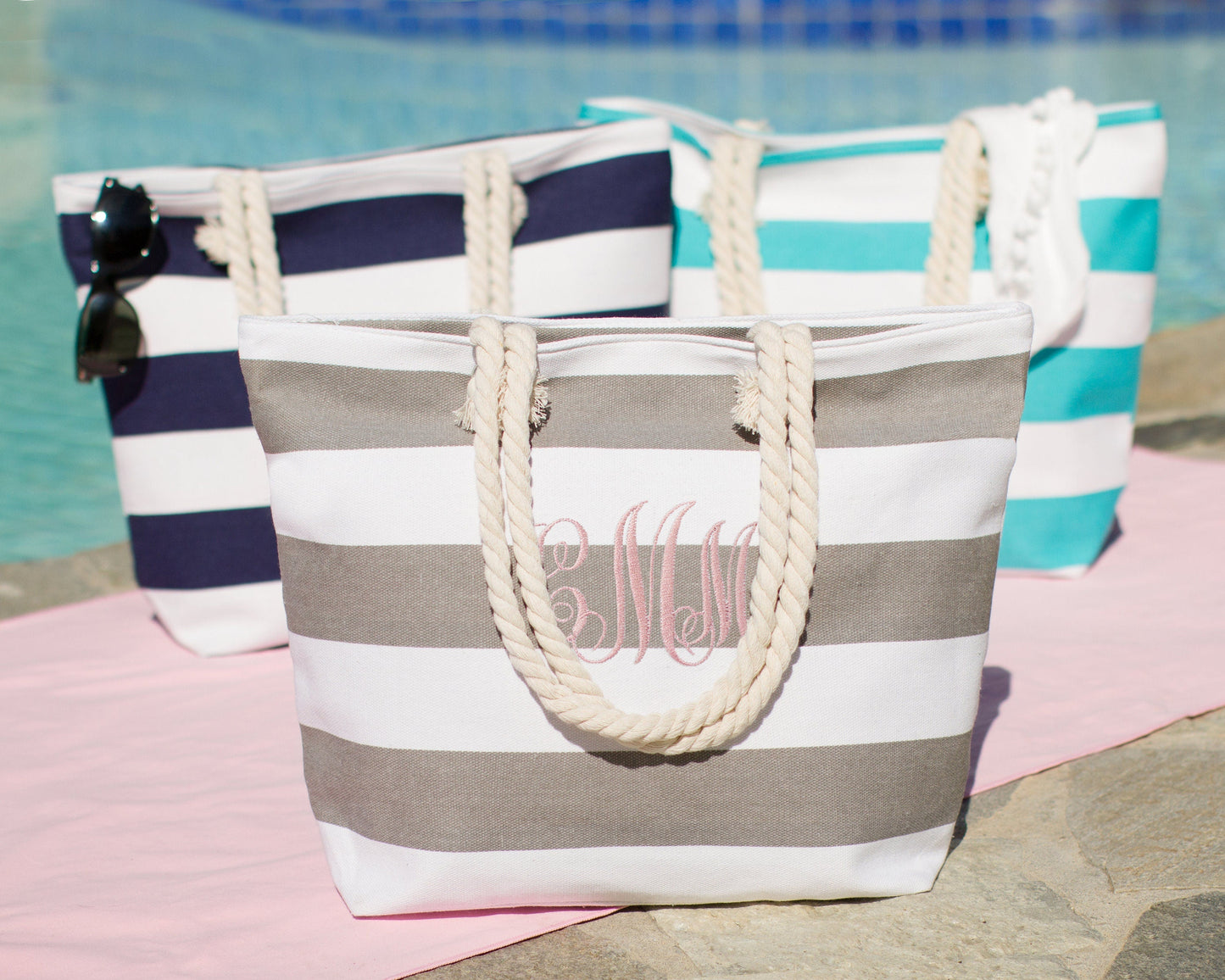 Gray, navy and turquoise bold stripe beach totes together beside a pool with sunglasses and a towel