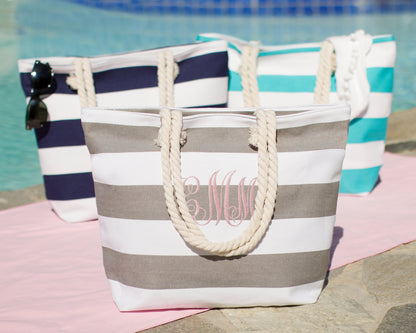 Gray, navy and turquoise bold stripe beach totes together beside a pool with sunglasses and a towel