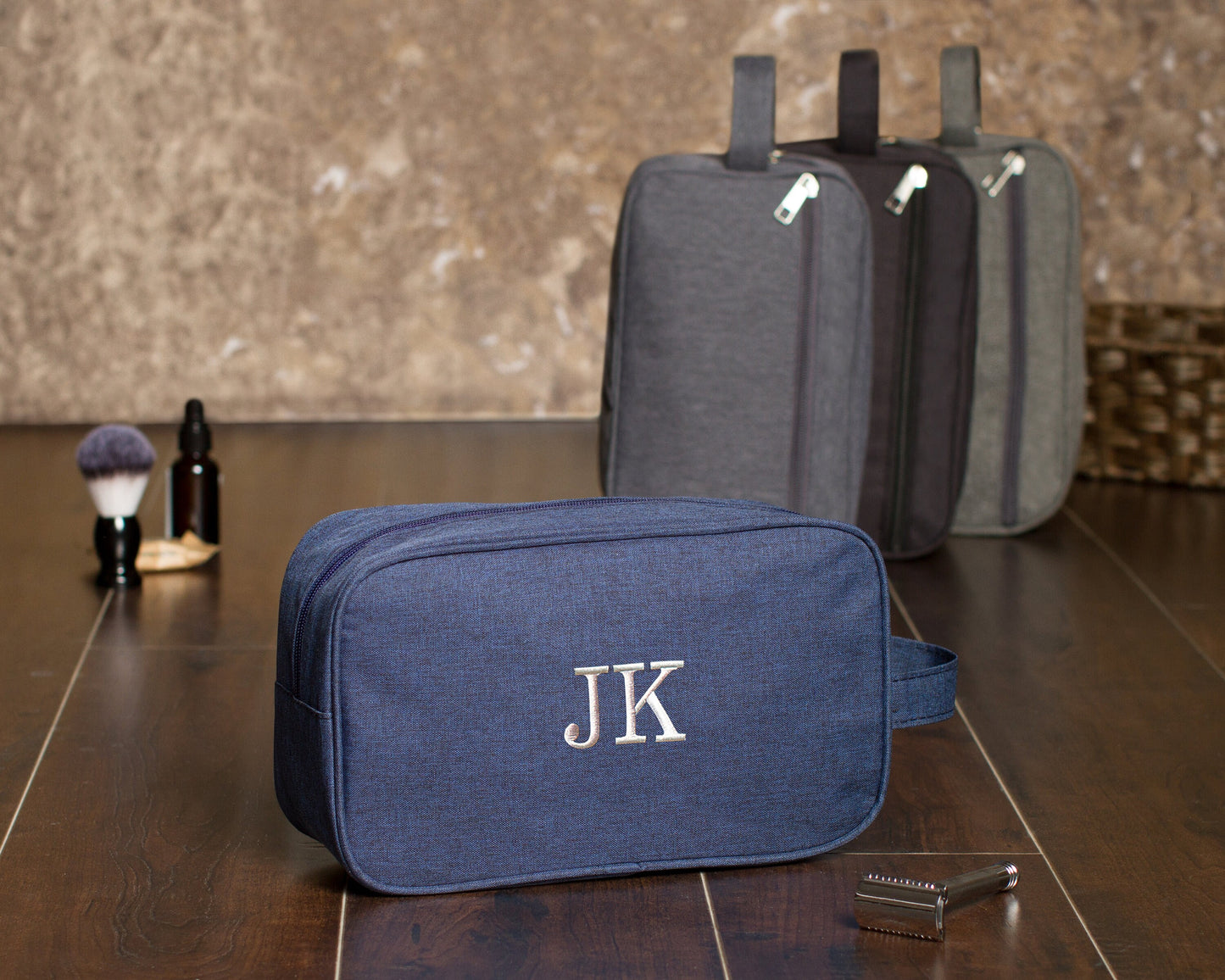 Navy dopp kit embroidered "JK" in front of three gray and charcoal kits standing upright