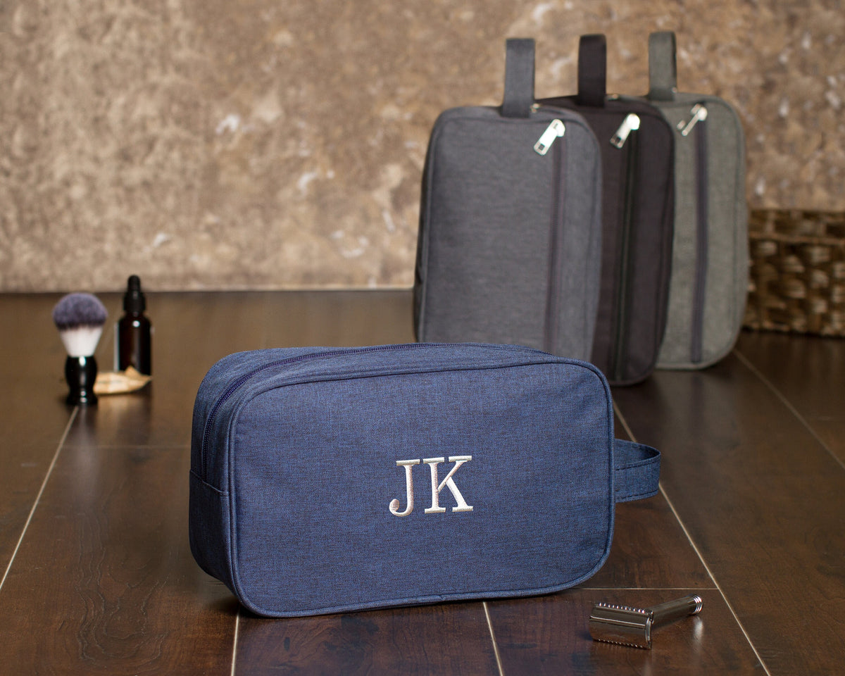 Navy dopp kit embroidered "JK" in front of three gray and charcoal kits standing upright