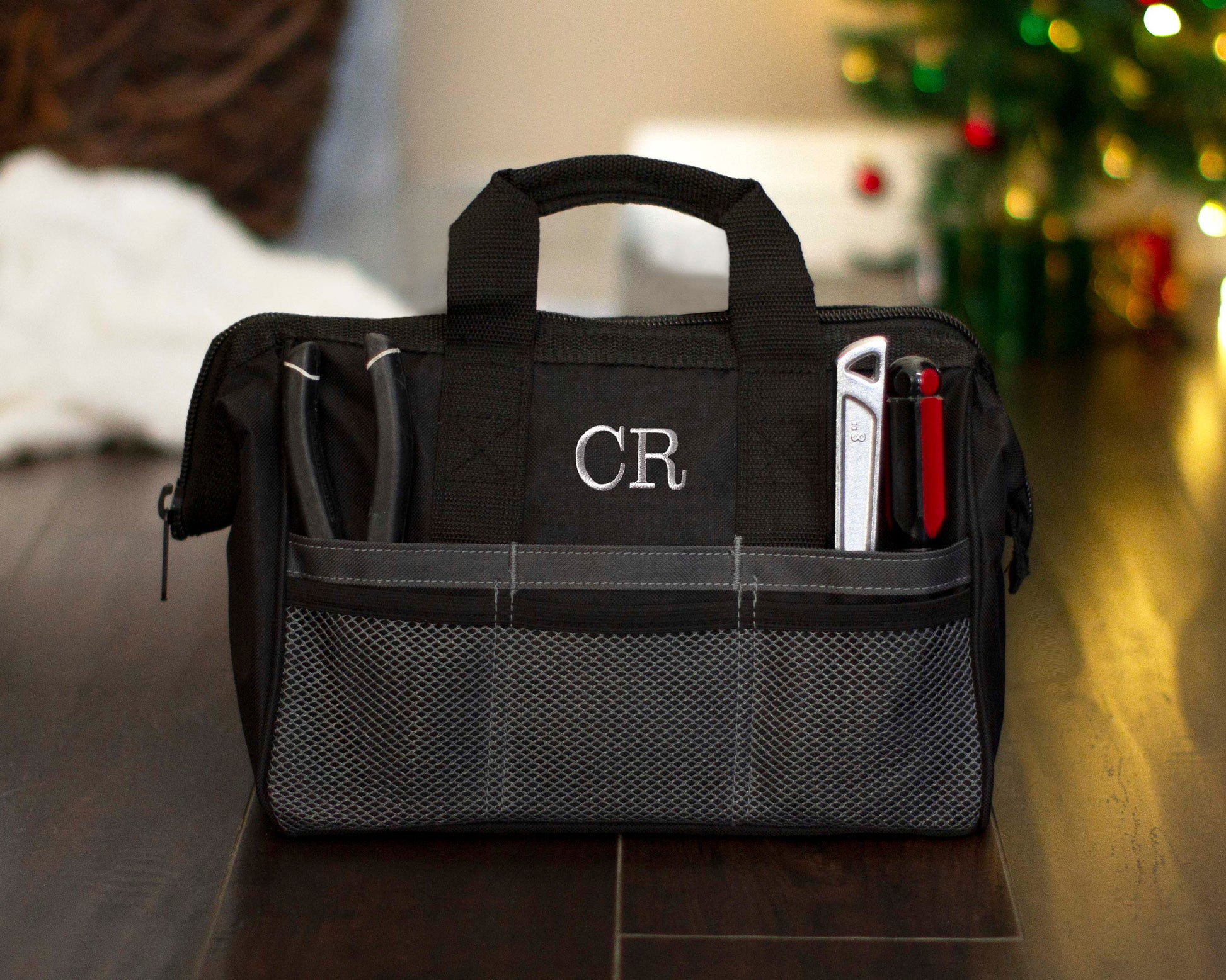Black tool bag embroidered with the monogram CR, tools stowed in the front pockets