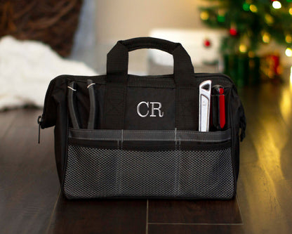 Black tool bag embroidered with the monogram CR, tools stowed in the front pockets