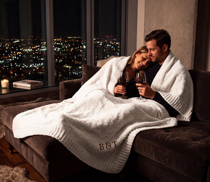 Couple on a sofa with a Moonstone cream Stargazer chenille throw featuring B & T embroidery.