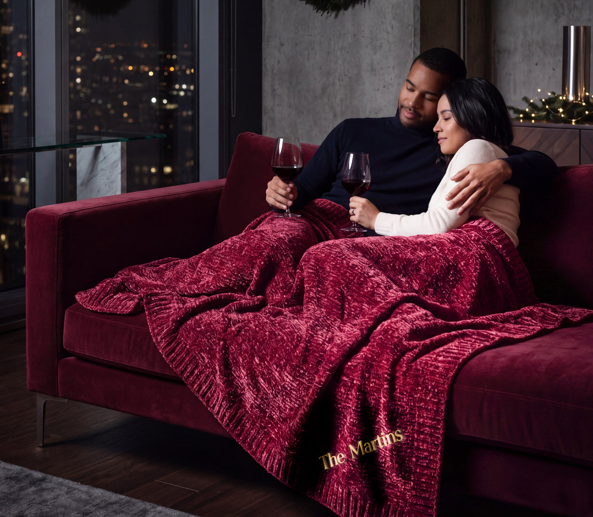 Nebula burgundy Stargazer chenille throw across a couple's laps, with The Martins embroidered near the ribbed edge.