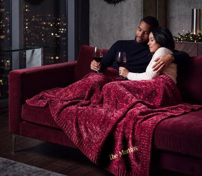 Nebula burgundy Stargazer chenille throw across a couple's laps, with The Martins embroidered near the ribbed edge.