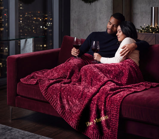 Nebula burgundy Stargazer chenille throw across a couple's laps, with The Martins embroidered near the ribbed edge.