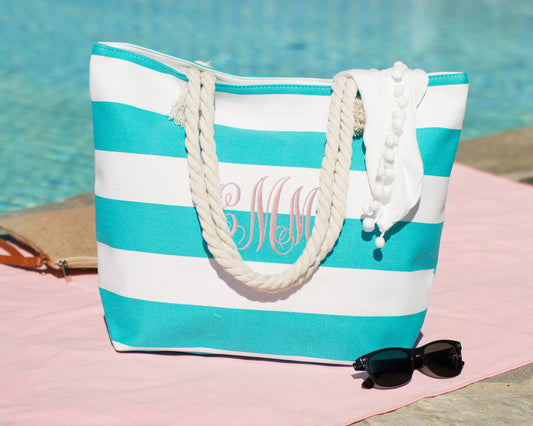 Turquoise and white bold stripe beach tote with a monogram, poolside on a towel with sunglasses