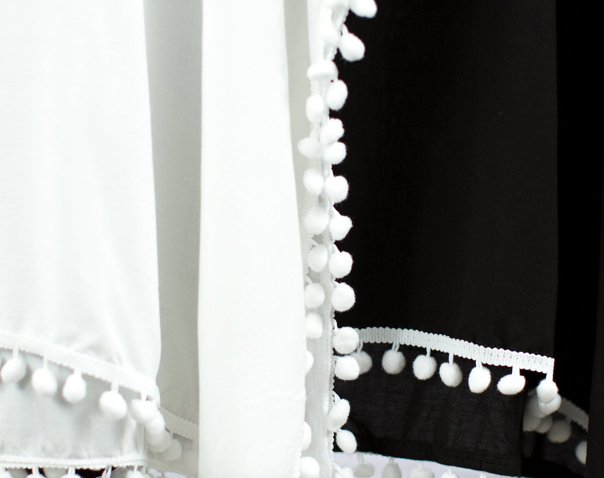 Close-up of the white pom-pom trim on the white and black cover-ups