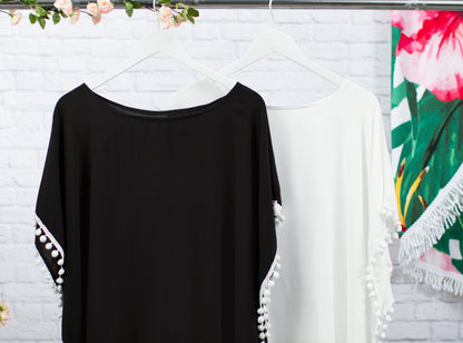 Black and white cover-ups hanging side by side against a white brick wall, showing the loose one-size drape