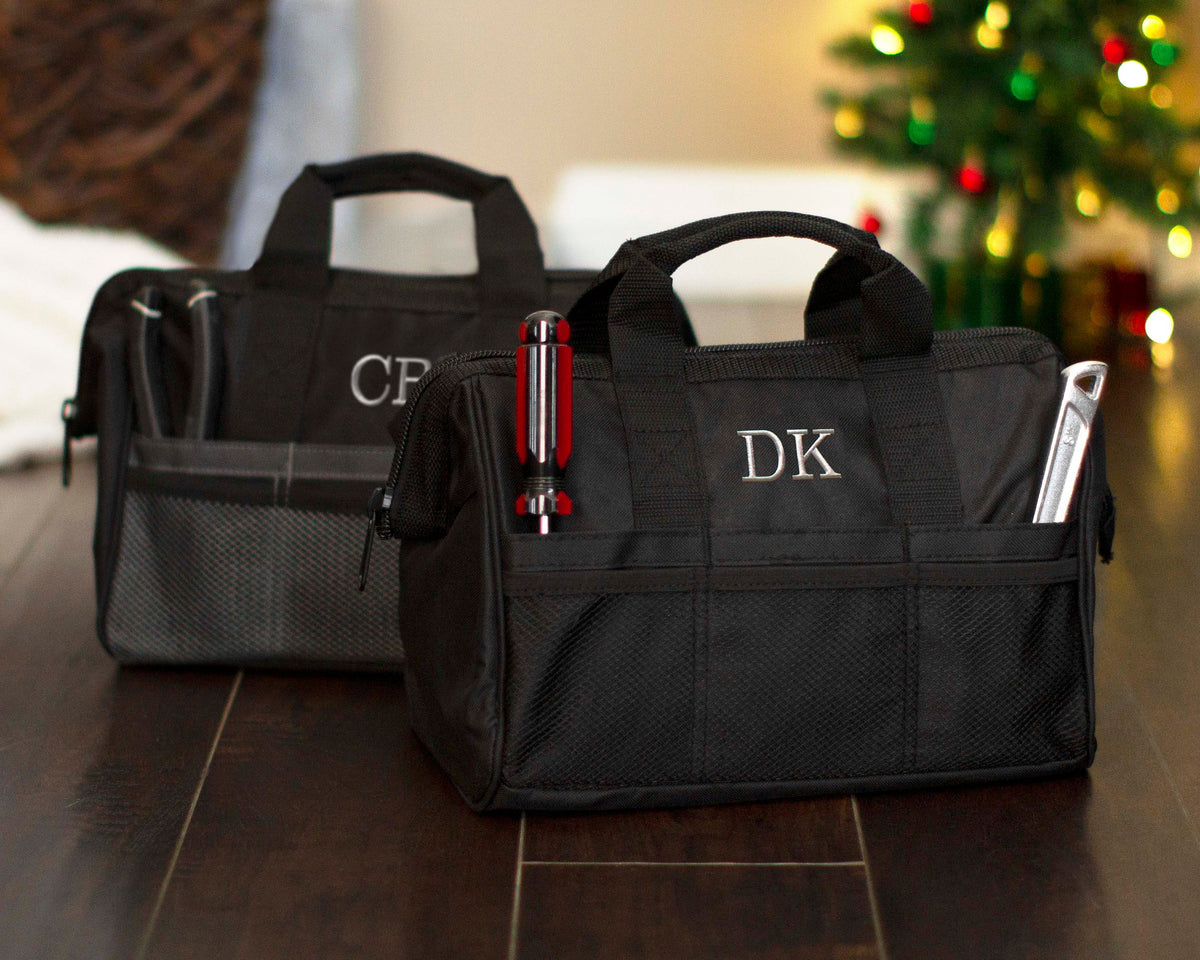 Personalized black tool bag with embroidered initials photographed on a wood floor