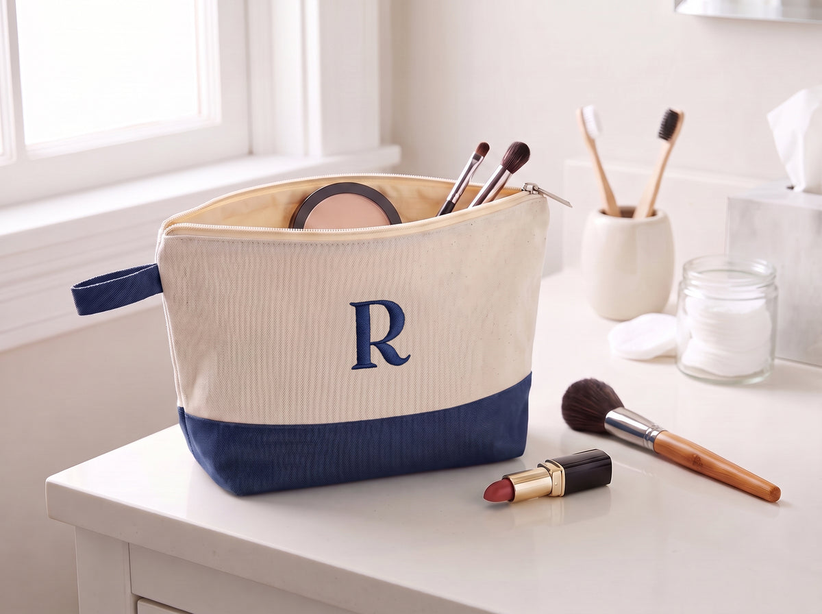 Open cream and navy canvas cosmetic bag with an embroidered R monogram on a bathroom vanity.