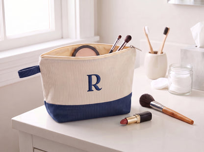 Open cream and navy canvas cosmetic bag with an embroidered R monogram on a bathroom vanity.