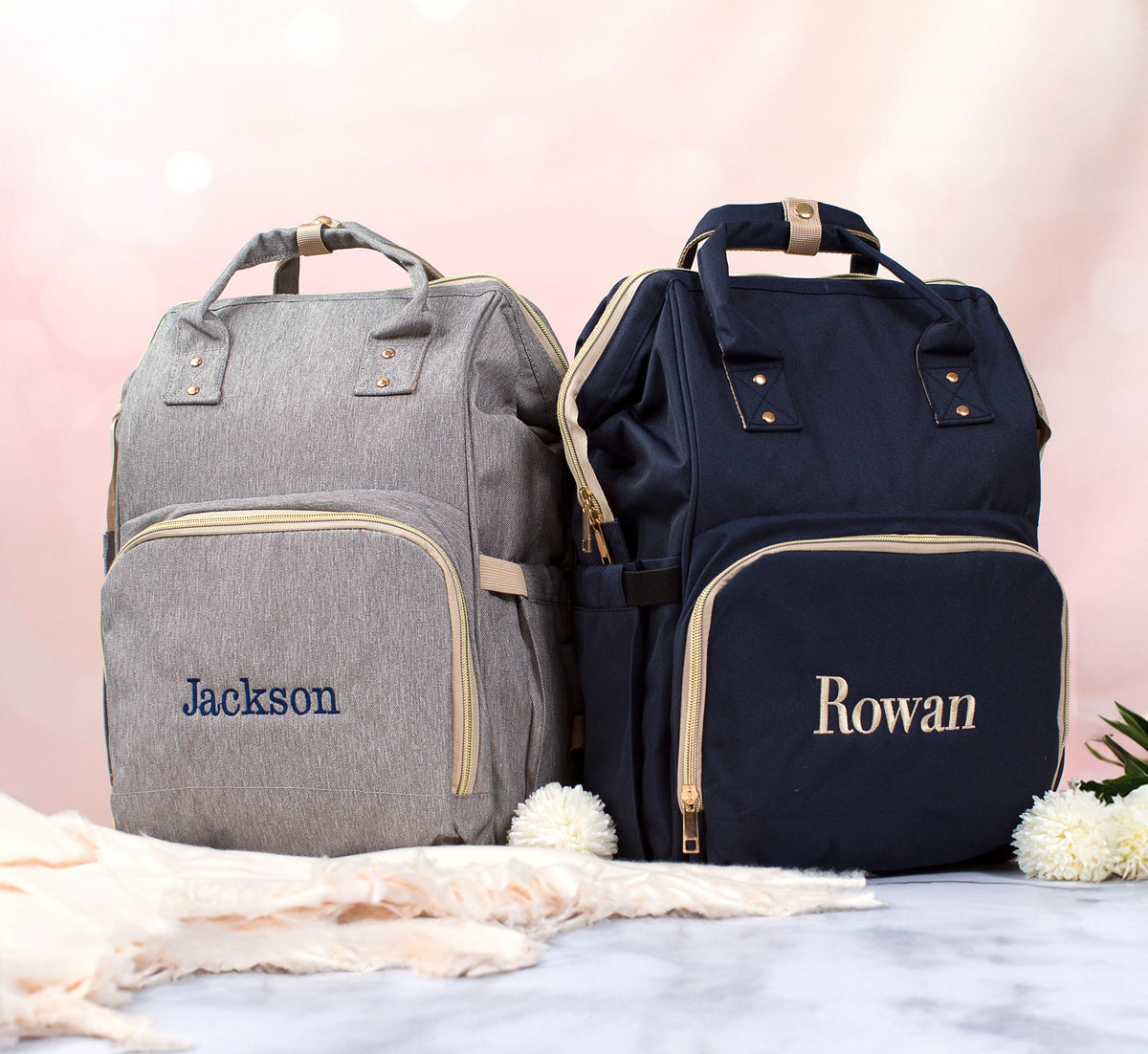 The Nursery Run Diaper Backpack — gray and navy embroidered with the baby names Jackson and Rowan