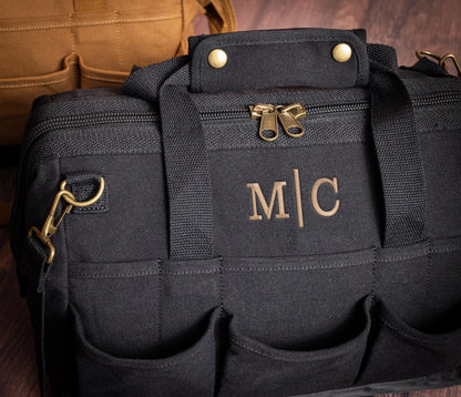 Black canvas tool bag with a monogram above its layered front pockets.