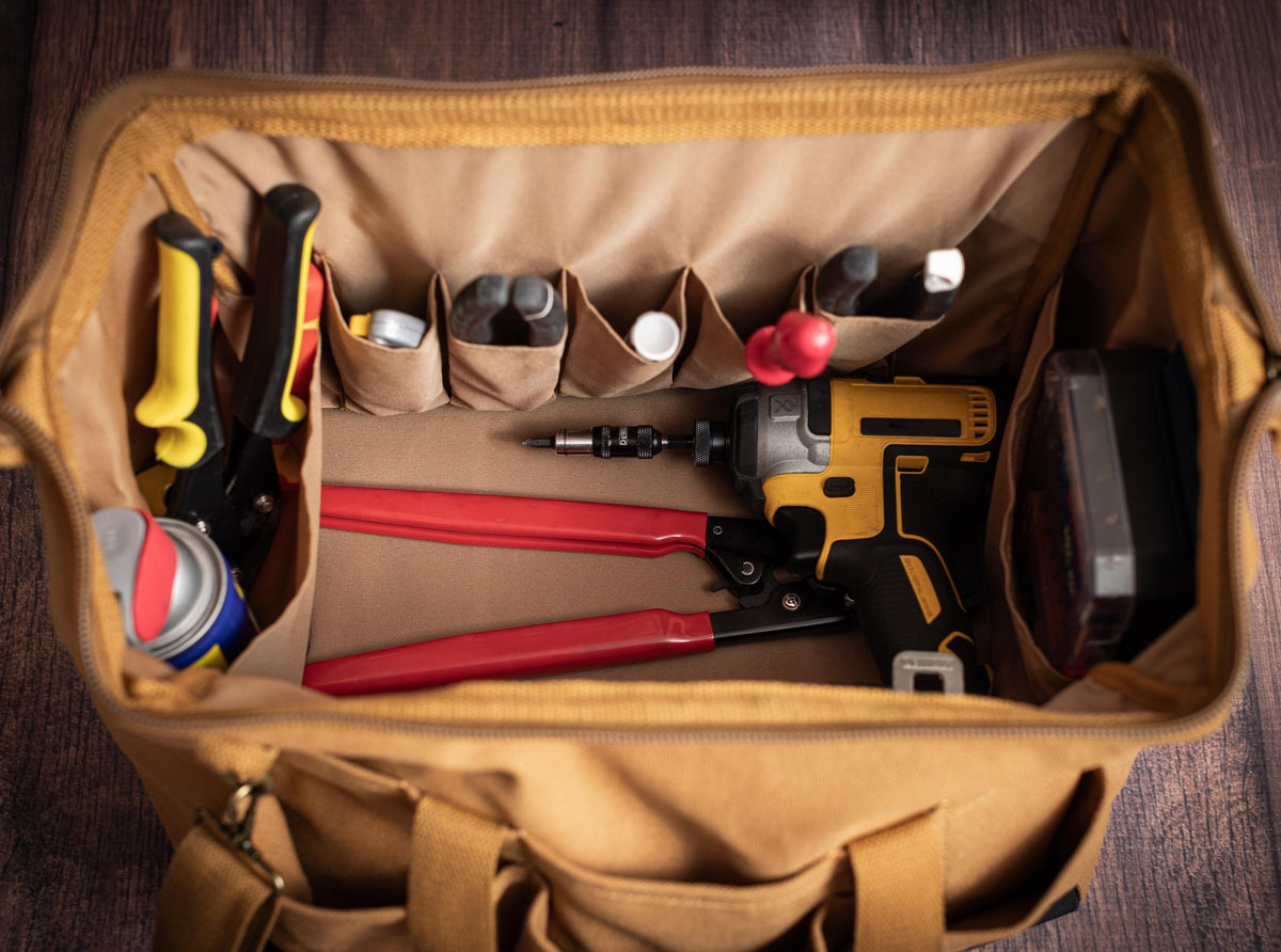 Open canvas tool bag showing its wide frame opening, interior pockets and hand tools.