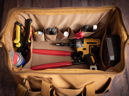 Open canvas tool bag showing its wide frame opening, interior pockets and hand tools.