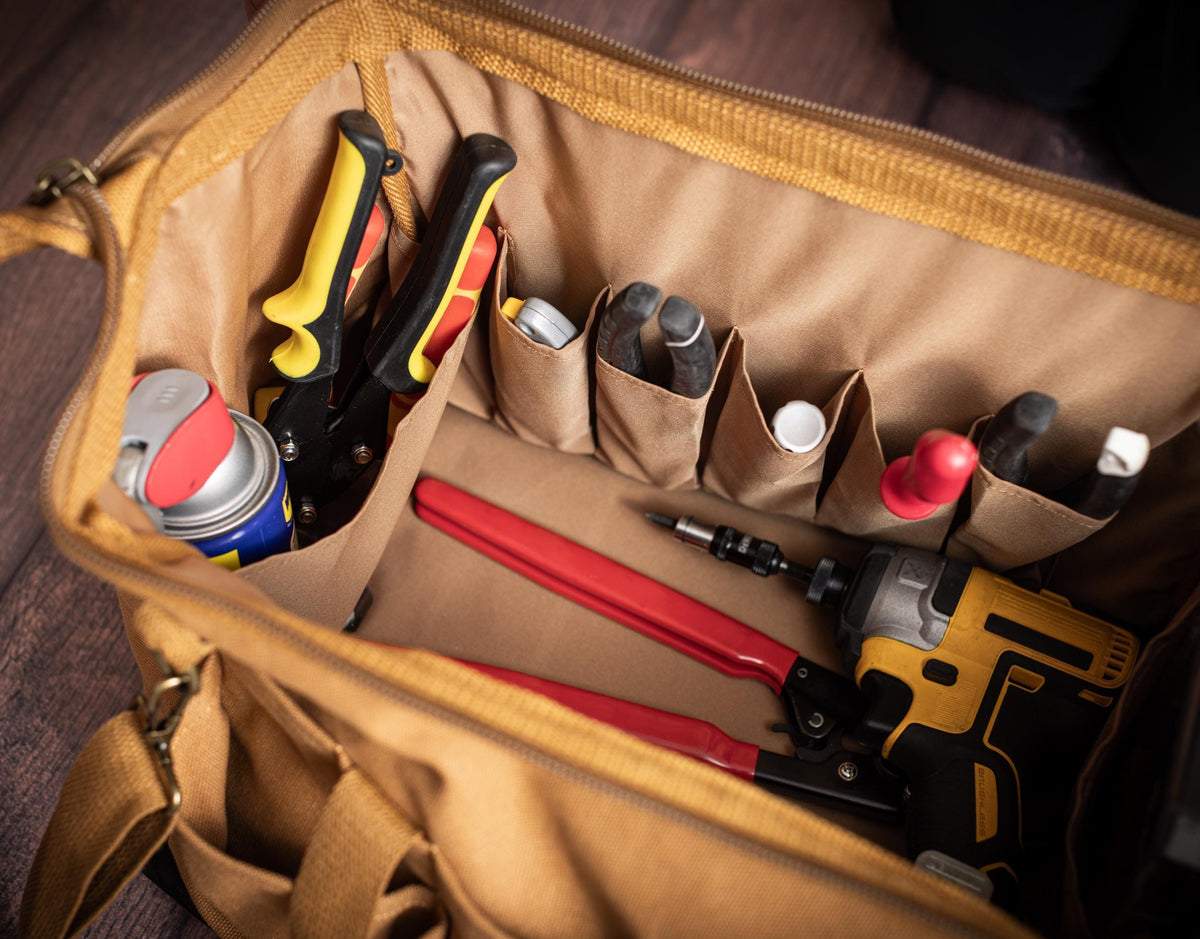 Brown canvas tool bag open with hand tools arranged in its main compartment and organizer pockets.