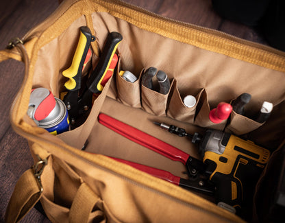 Brown canvas tool bag open with hand tools arranged in its main compartment and organizer pockets.